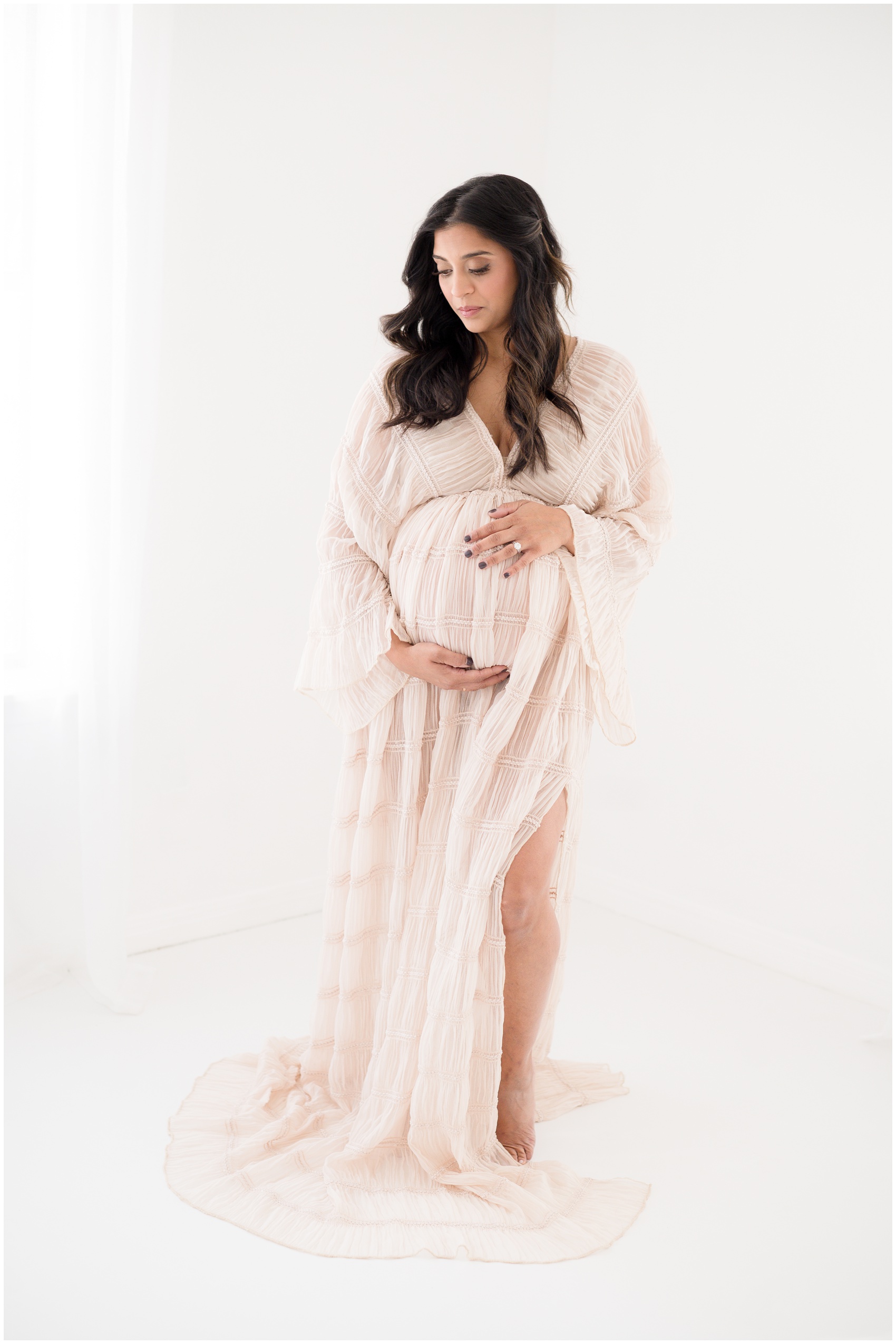 A pregnant woman walks in a studio while holding her bump in a pink maternity gown after meeting doulas in austin