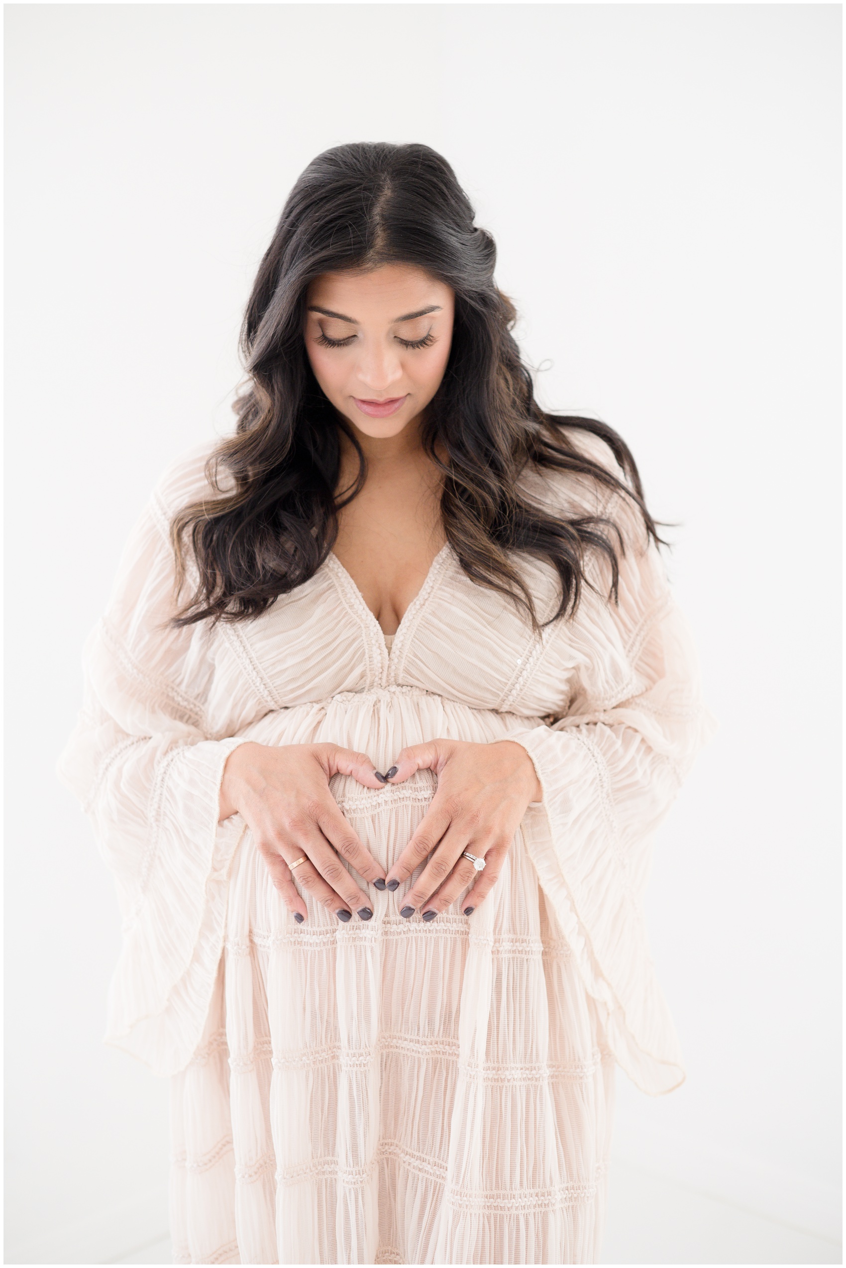 A mom to be makes a heart on her bump in a pink maternity gown in a studio after meeting doulas in austin