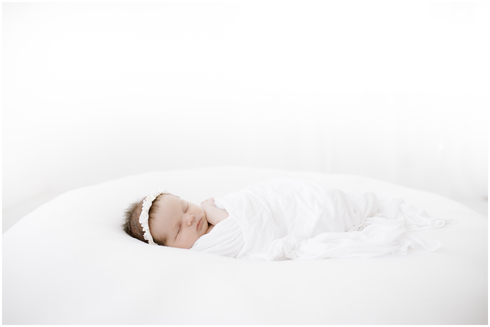 A newborn baby sleeps on a bean bag under a white blanket with a matching headband after meeting a night nurse in austin