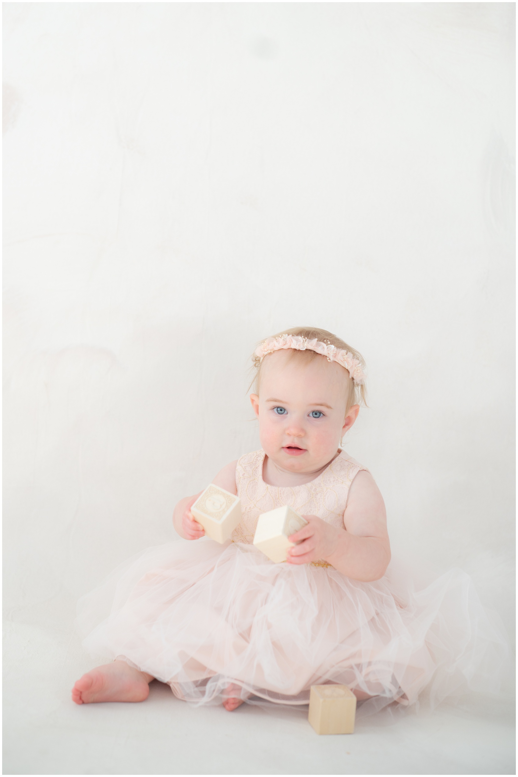 A toddler girl plays with wooden blocks on the floor of a studio in a pink dress after visiting parks in austin for kids