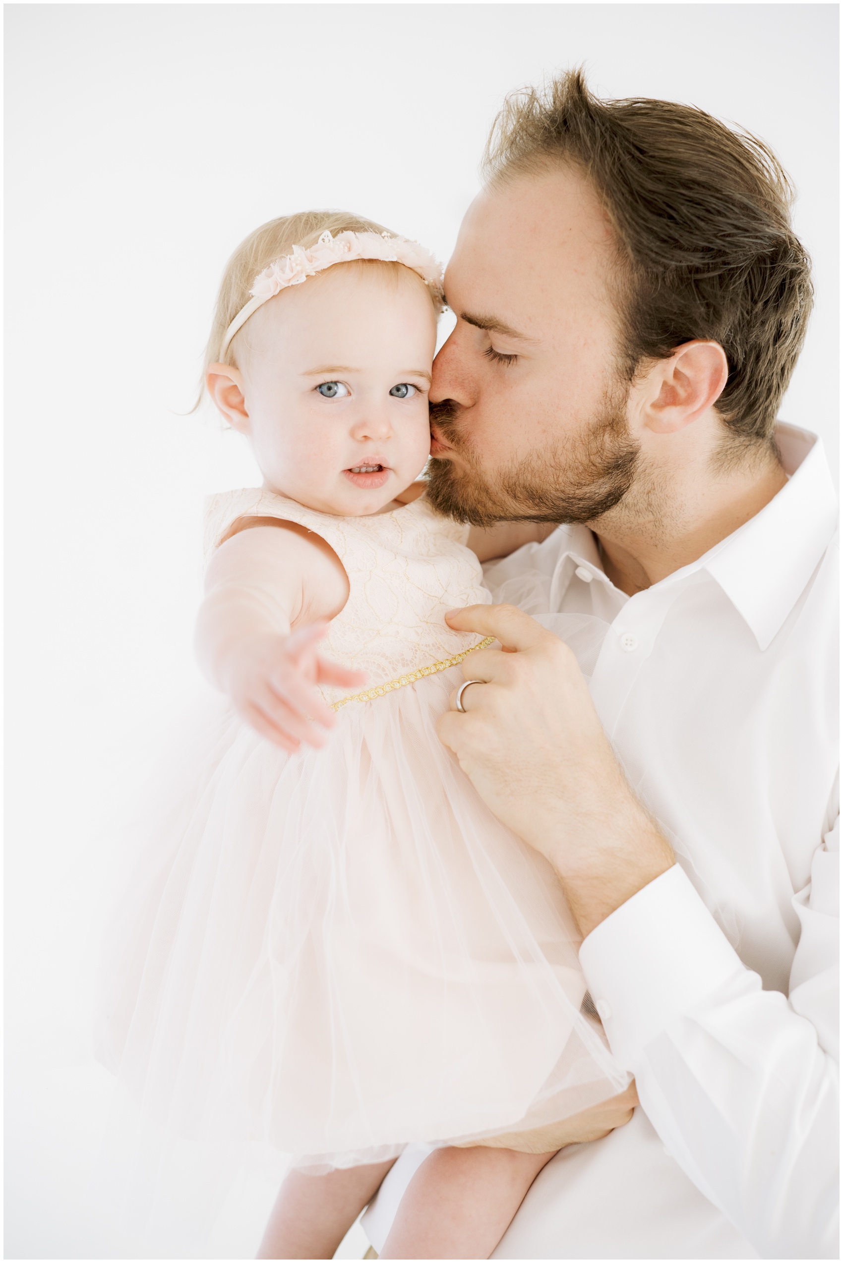 A father kisses the cheek of his toddler daughter in a yellow dress before visiting parks in austin for kids