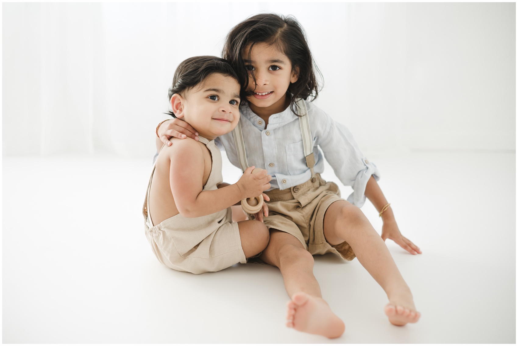 Young toddler boys sit on a studio floor hugging and smiling before visiting toy stores in austin