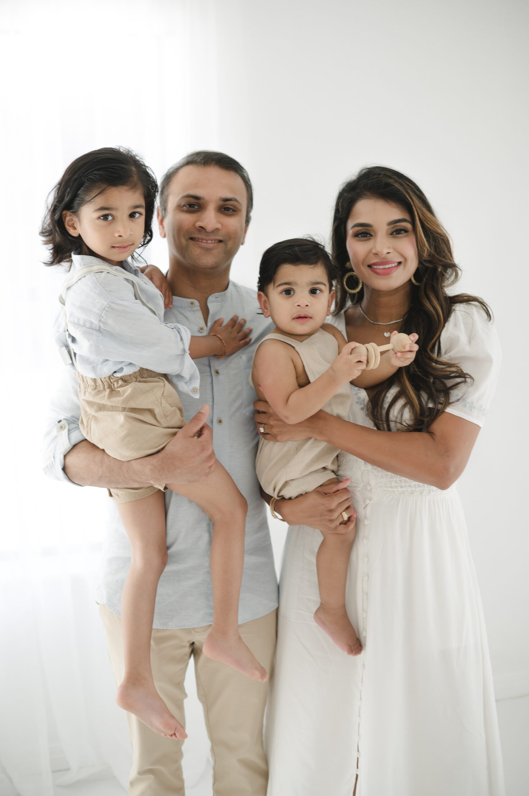 Happy mom and dad stand in a studio holding their toddler and baby sons in their arms after visiting an austin pediatrician