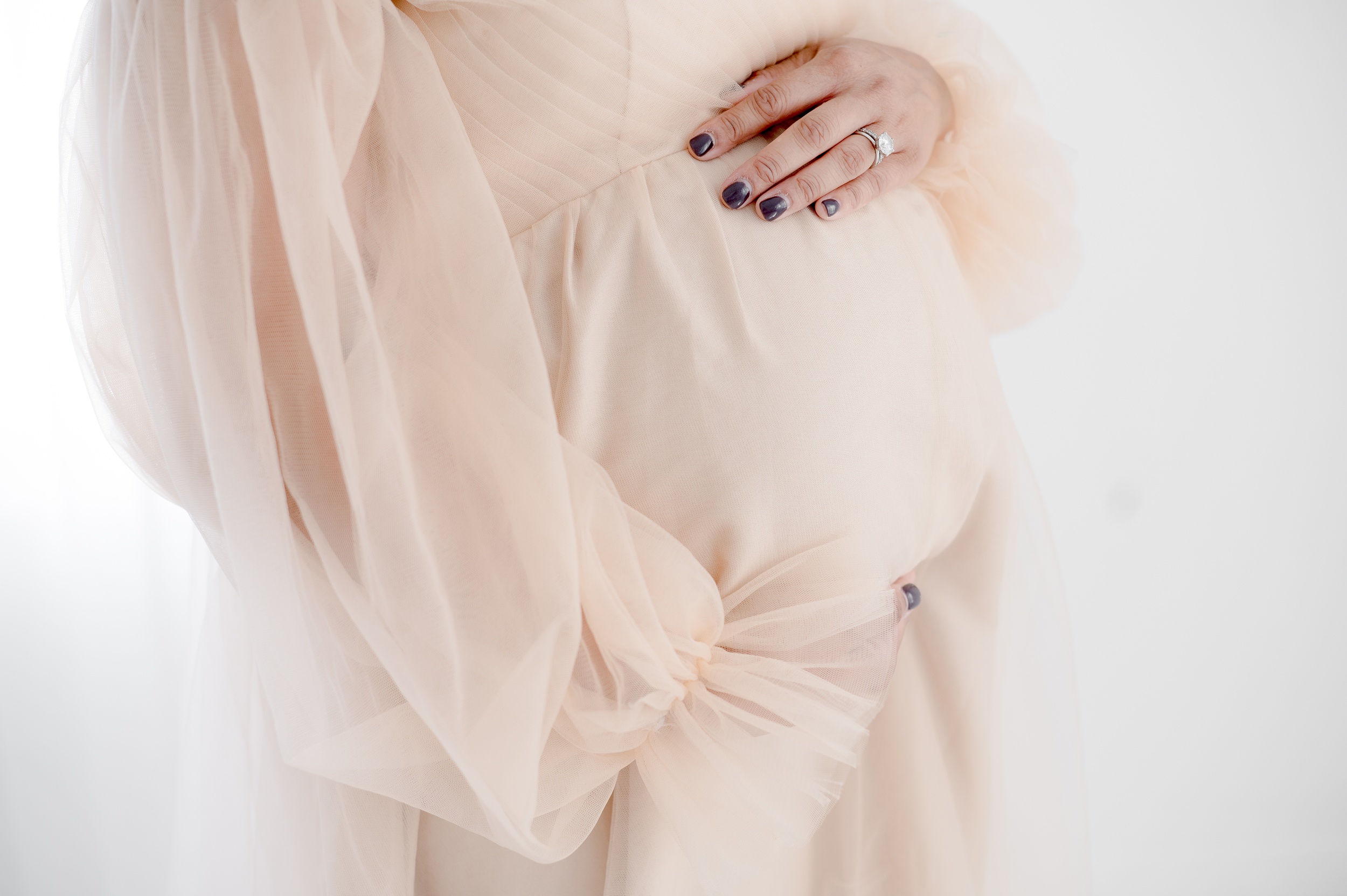 Details of a mom to be's hands on her bump in a pink maternity gown after visiting an obgyn in austin