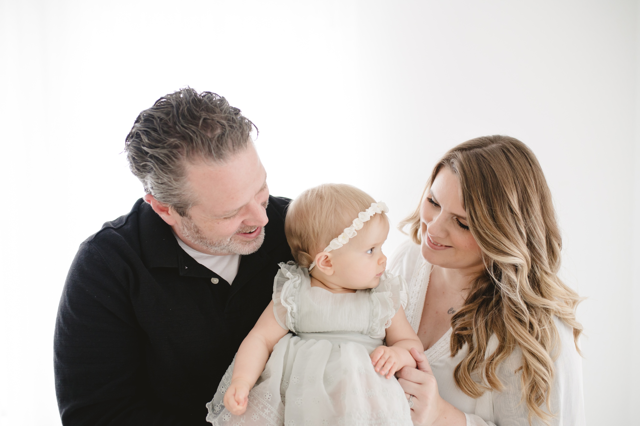 Happy mom and dad admire their daughter sitting in their hands in a dress in a studio after some parenting classes in austin