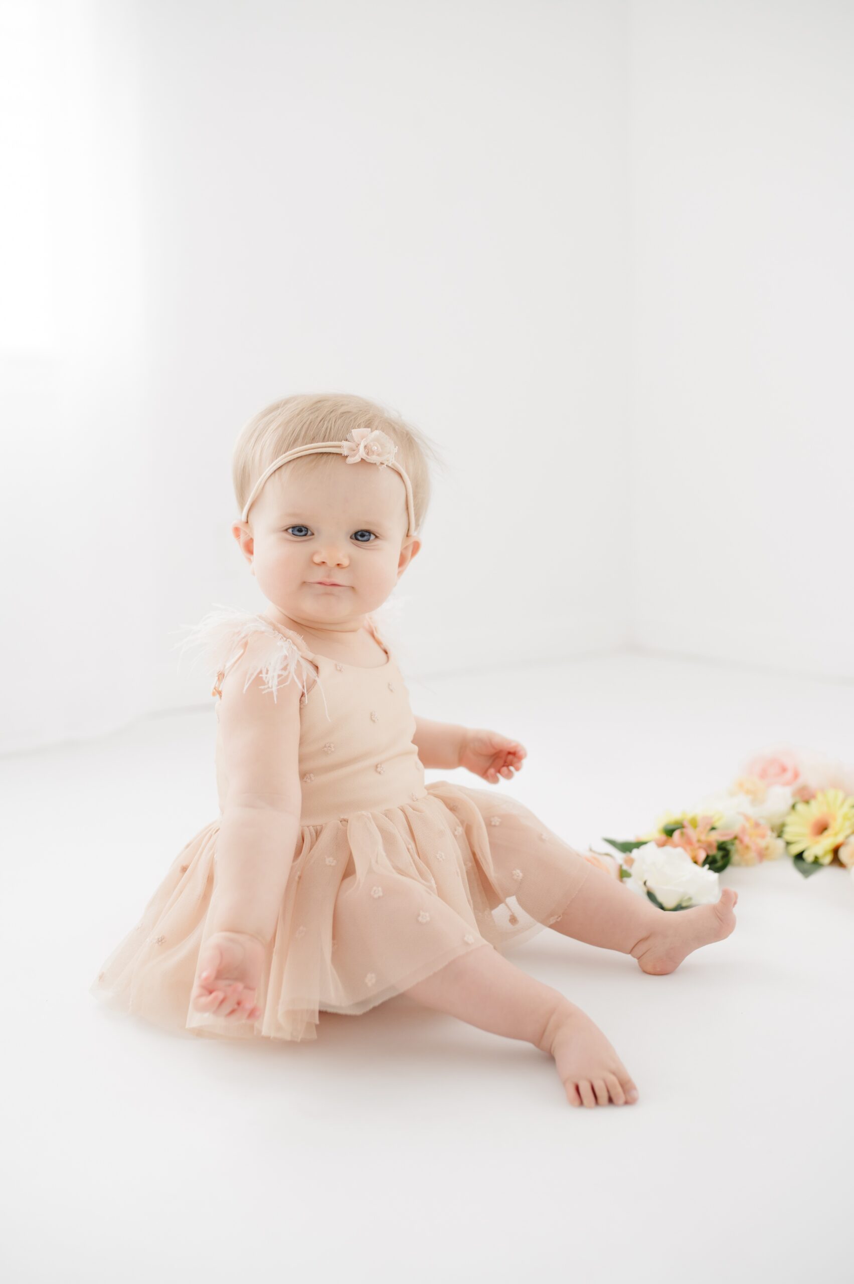 A baby sits in a studio in a cream dress with a smile after visiting preschools in austin