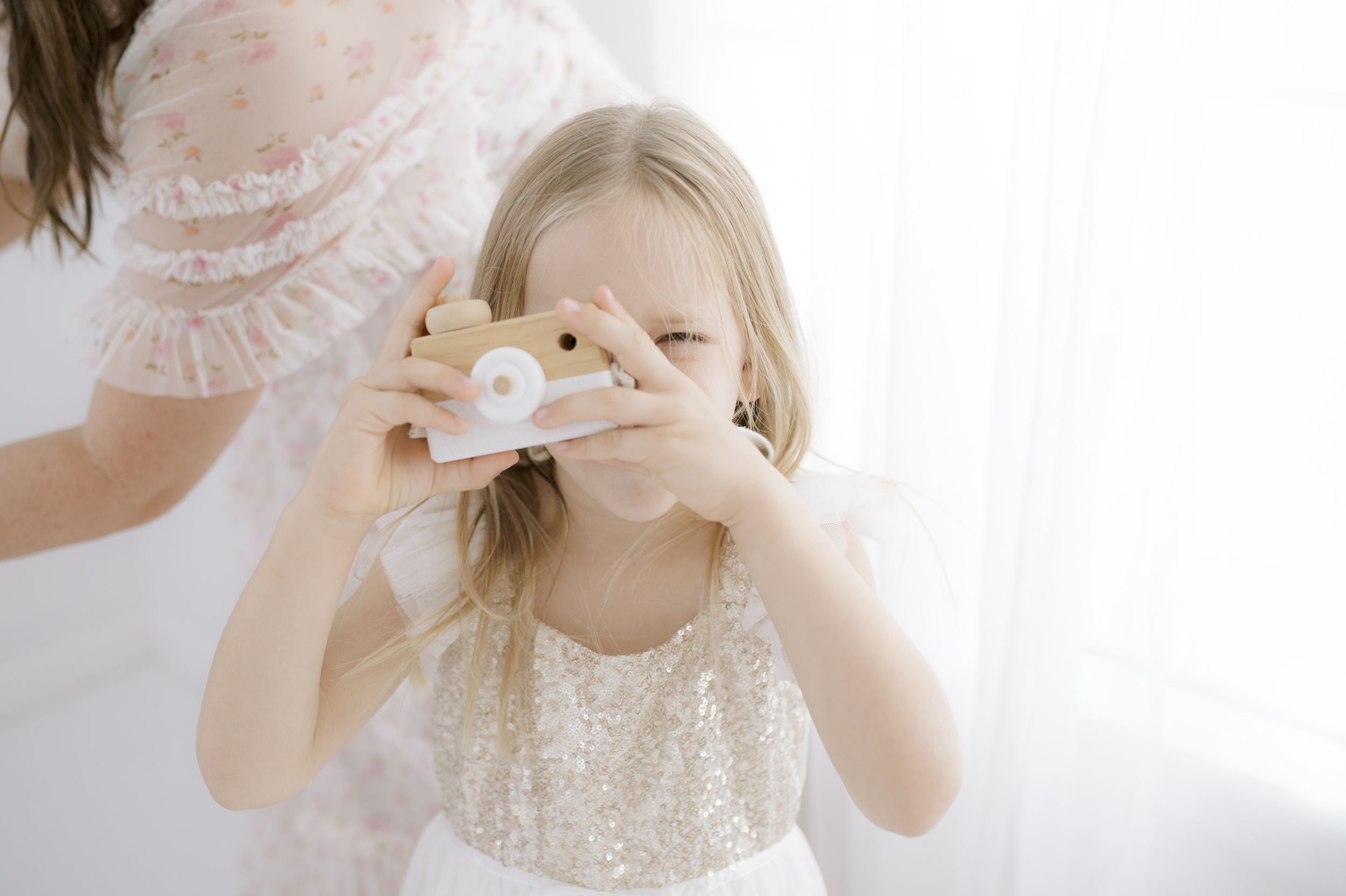 A young girl in a white dress plays with a wooden toy camera in a studio after meeting austin nanny agencies