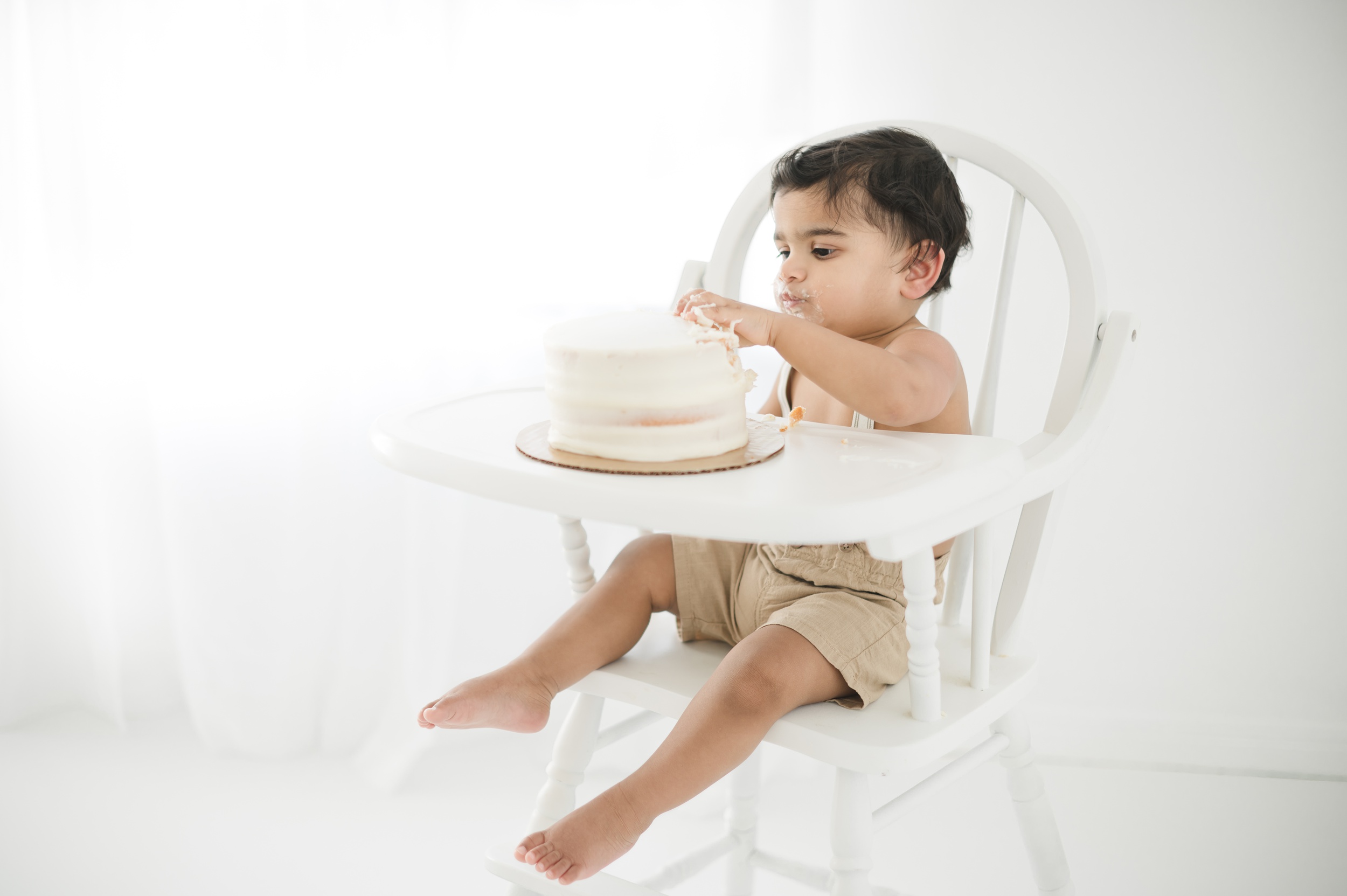 A happy baby eats a cake in a white highchair in a studio after some kids cooking classes in austin