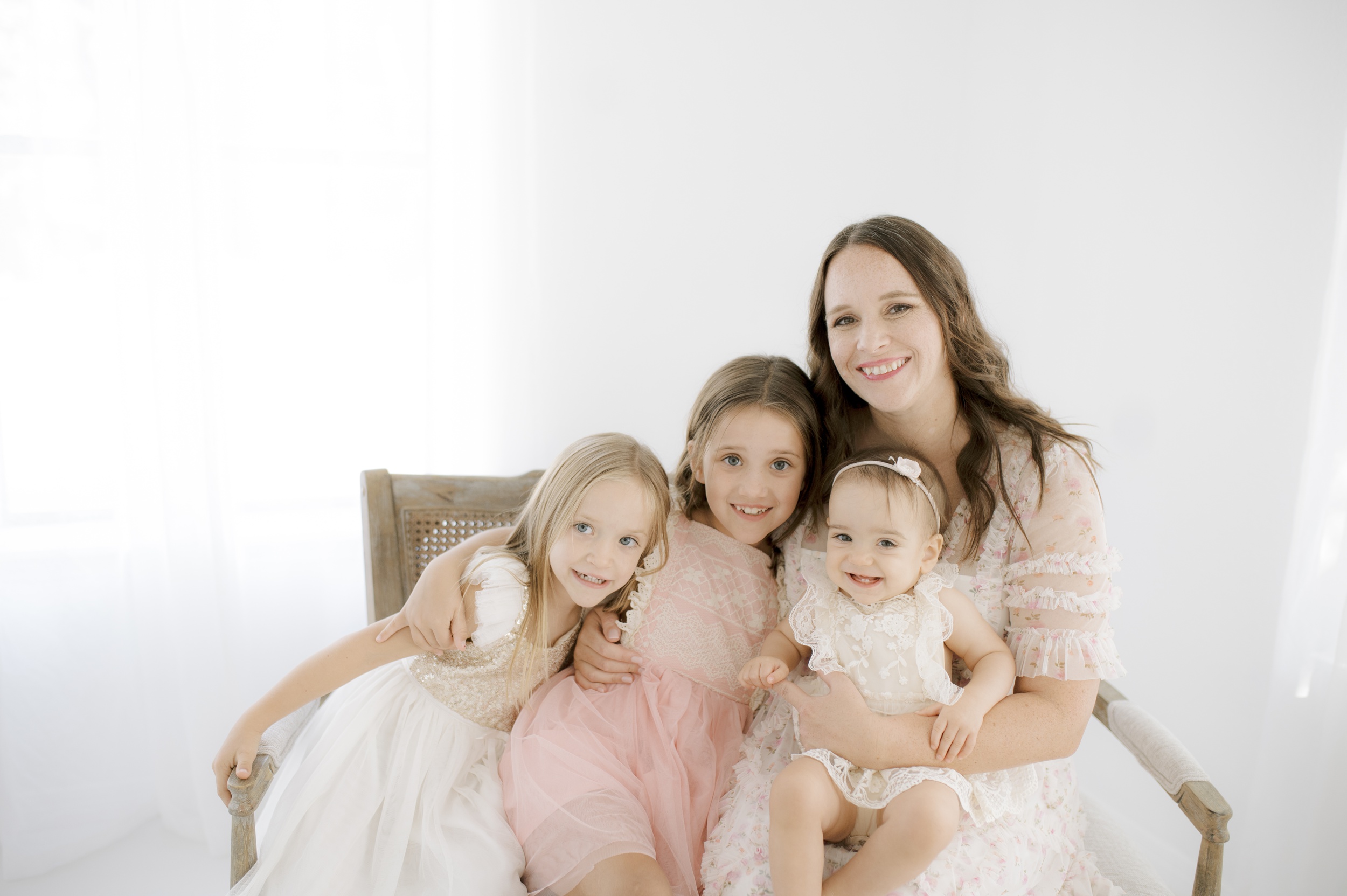 A happy mom sits in a studio bench hugging her three young daughters after going bowling for kids in austin