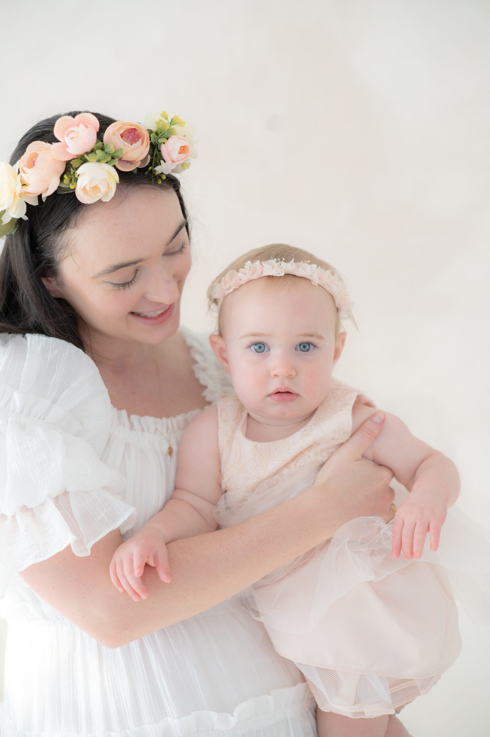 A baby girl in a pink dress sits in mom's arms in a studio after visiting kids dance studios in austin