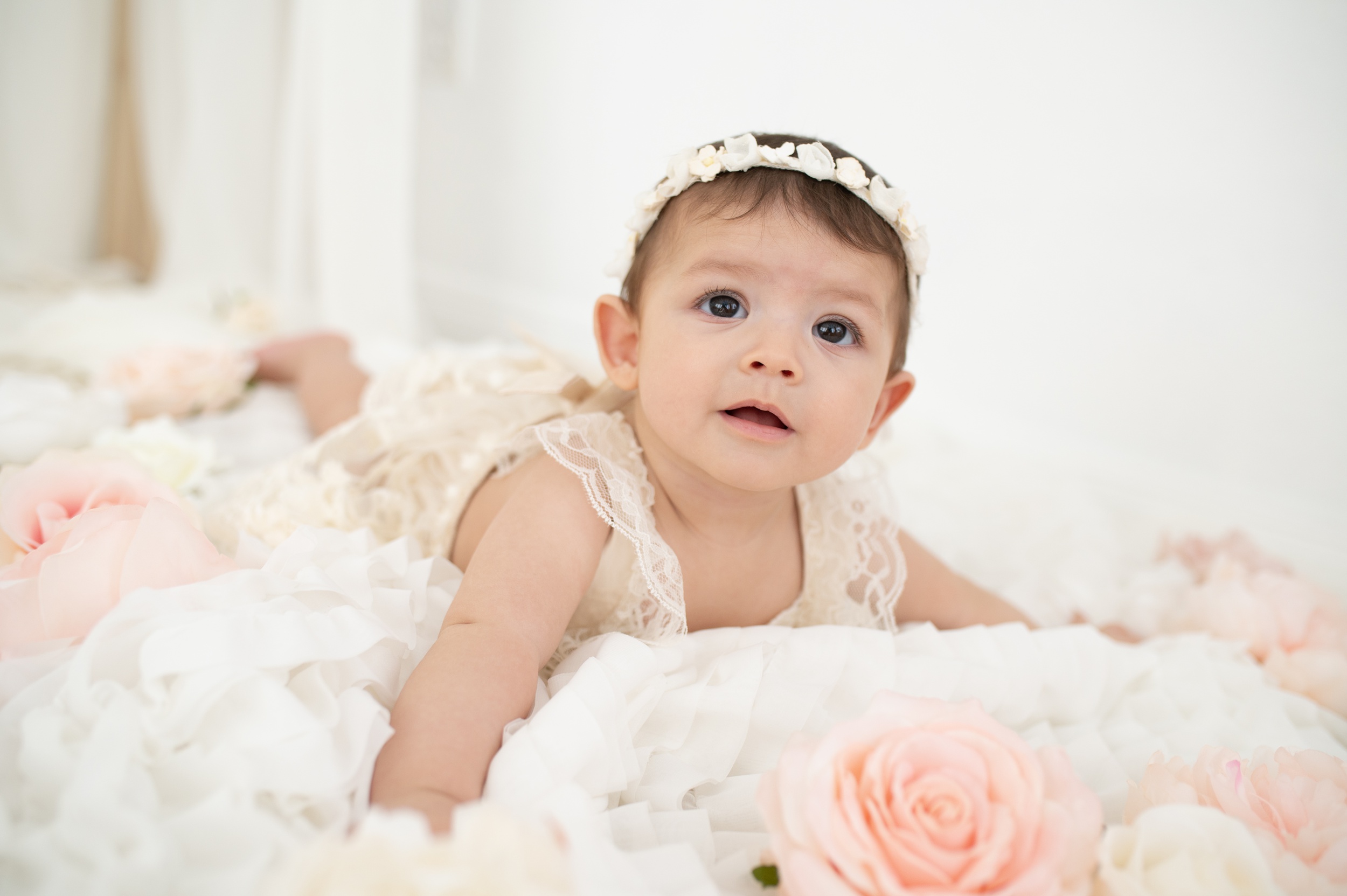 A baby girl in a white lace dress crawls on a bed after getting kids haircuts in austin