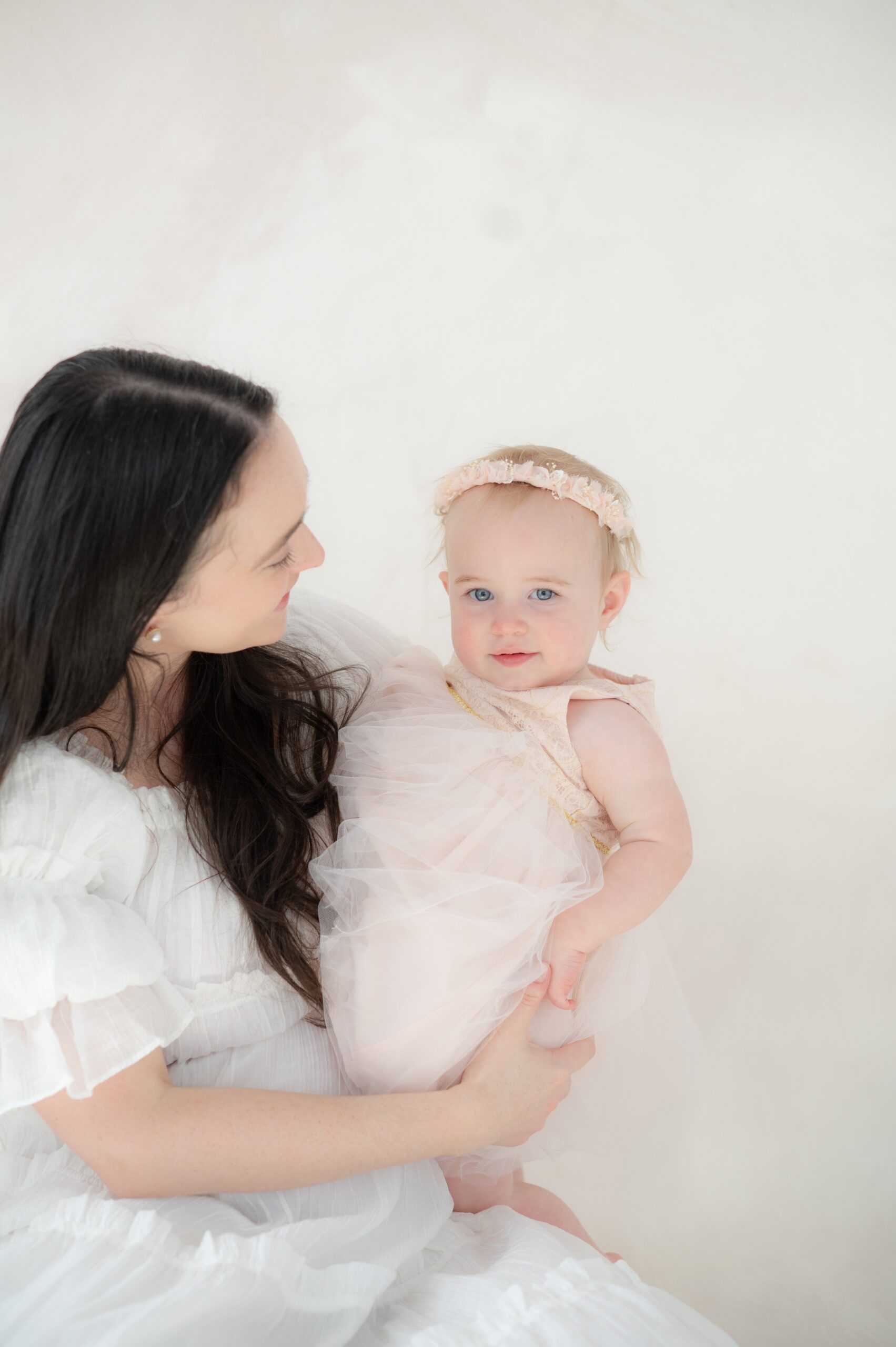 A happy mom sits with her infant daughter in her lap in a pink dress in a studio before Summer dance camps in austin