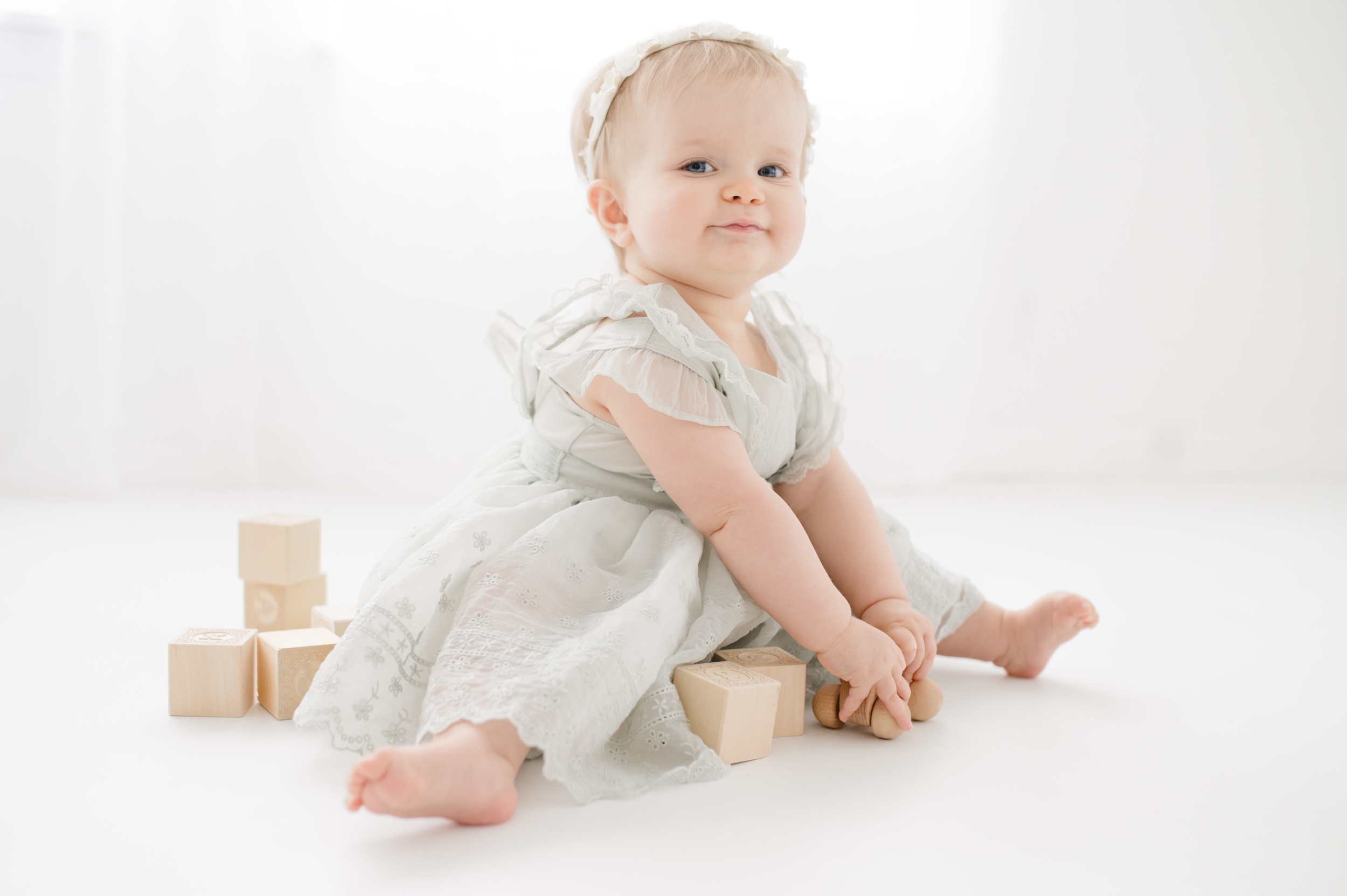 A happy baby girl plays with wooden toys on the floor of a studio before visiting summer gymnastics camps in austin