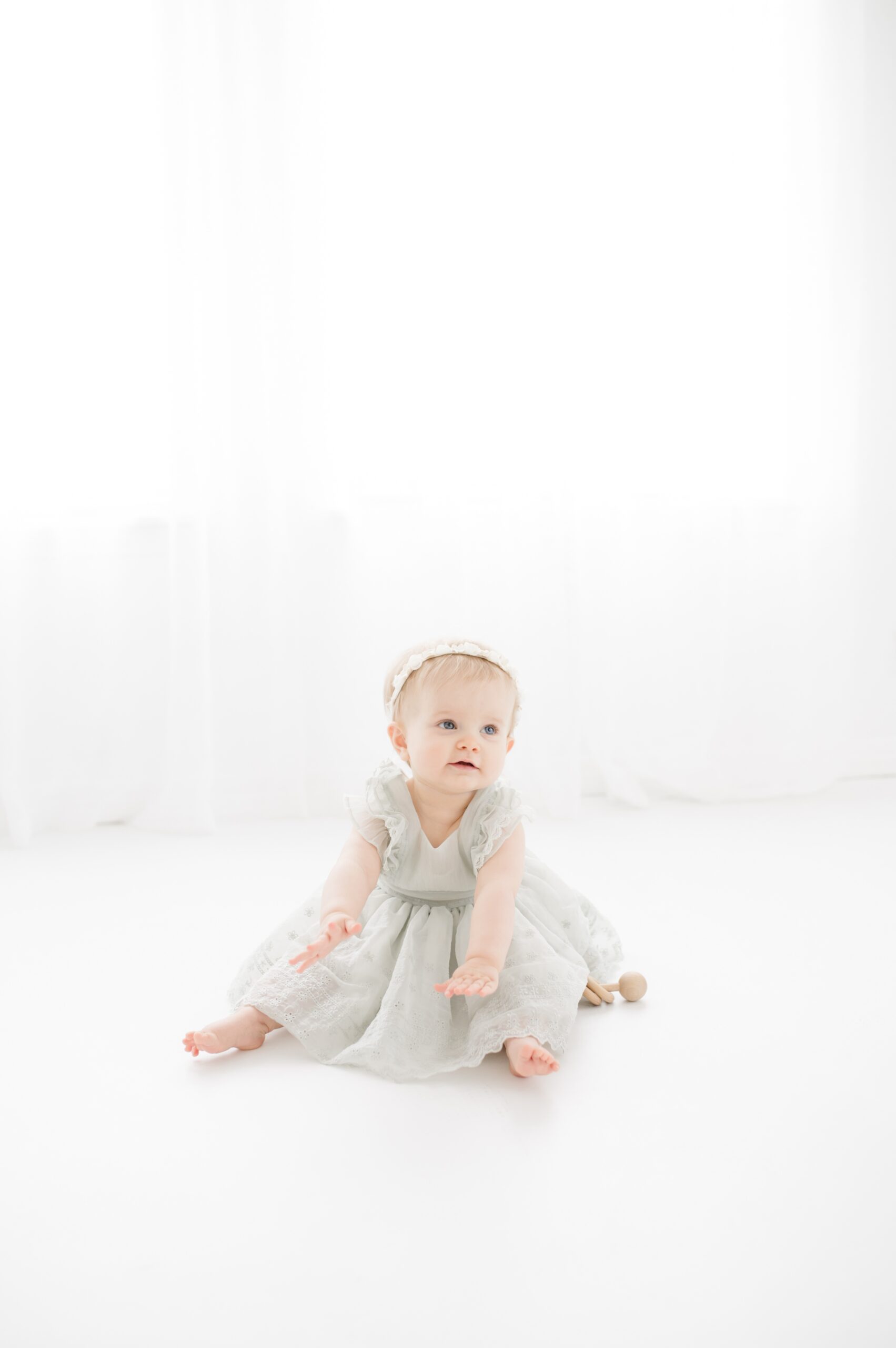 A baby girl in a dress plays on the floor of a studio under a window before summer gymnastics camps in austin