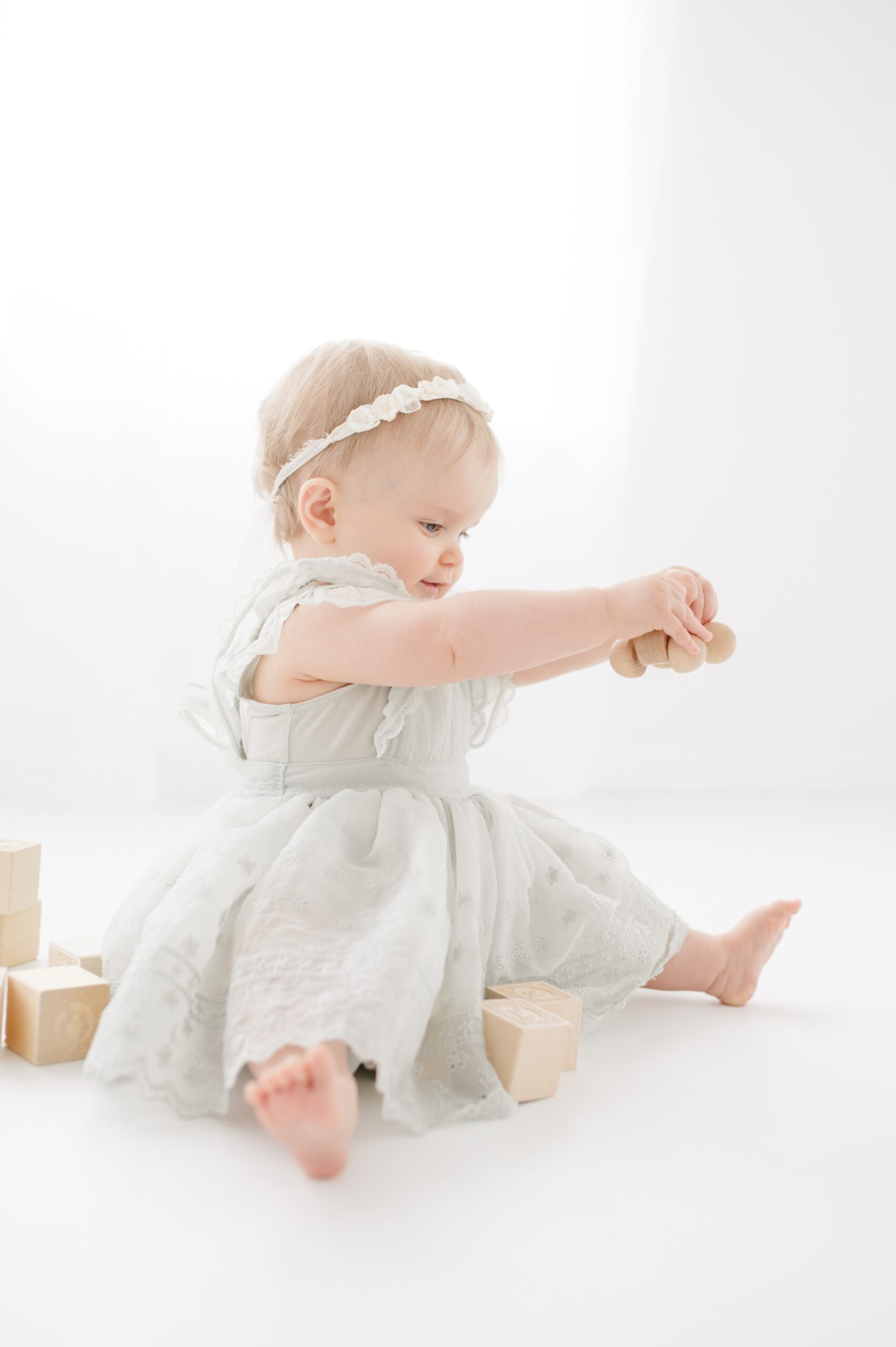 A baby girl sits in a studio playing with wooden toys in a dress and headband before visiting ice cream shops in Austin
