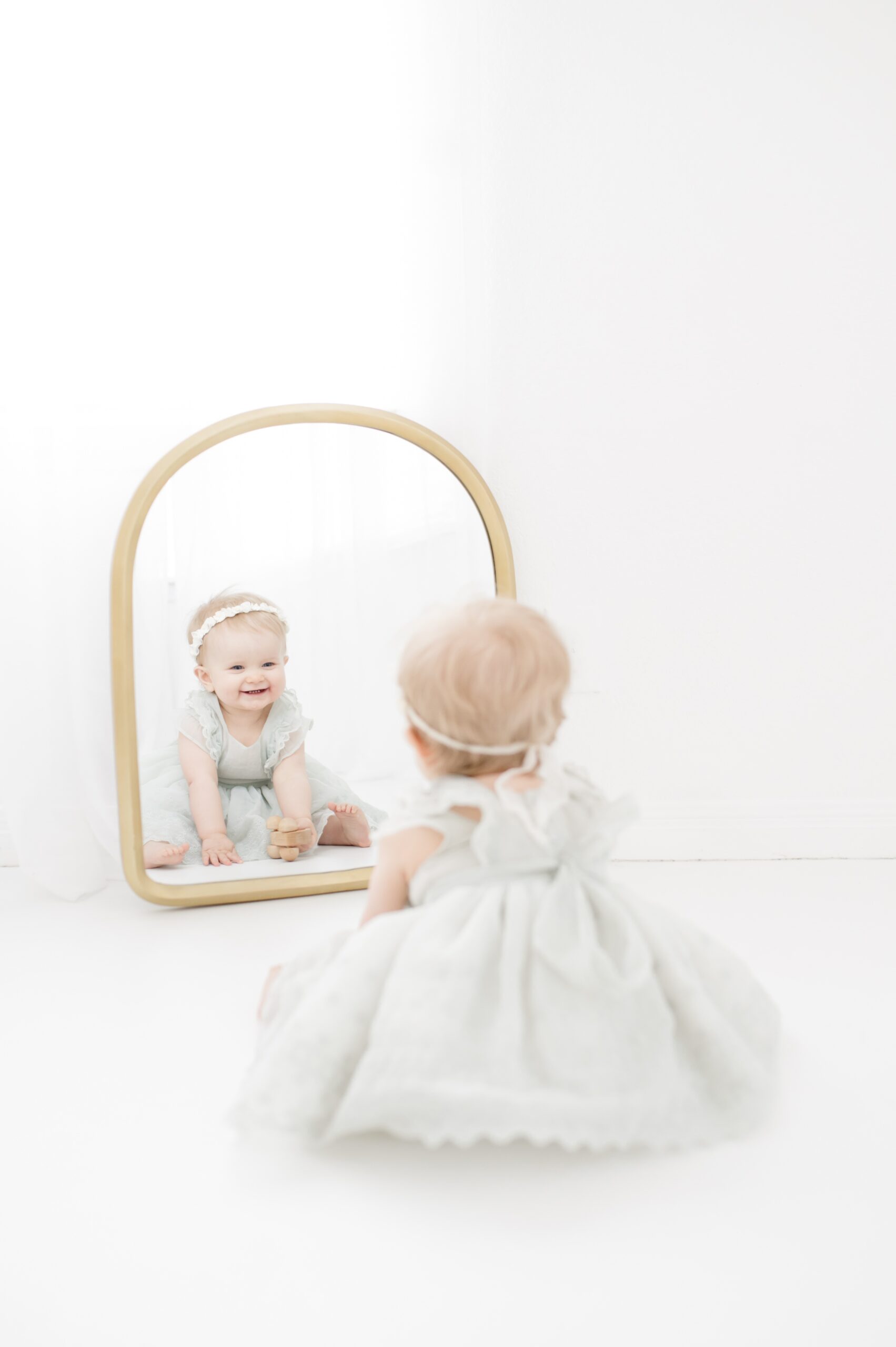 A giggling infant plays with herself in a mirror in a studio in a dress before visiting ice cream shops in Austin